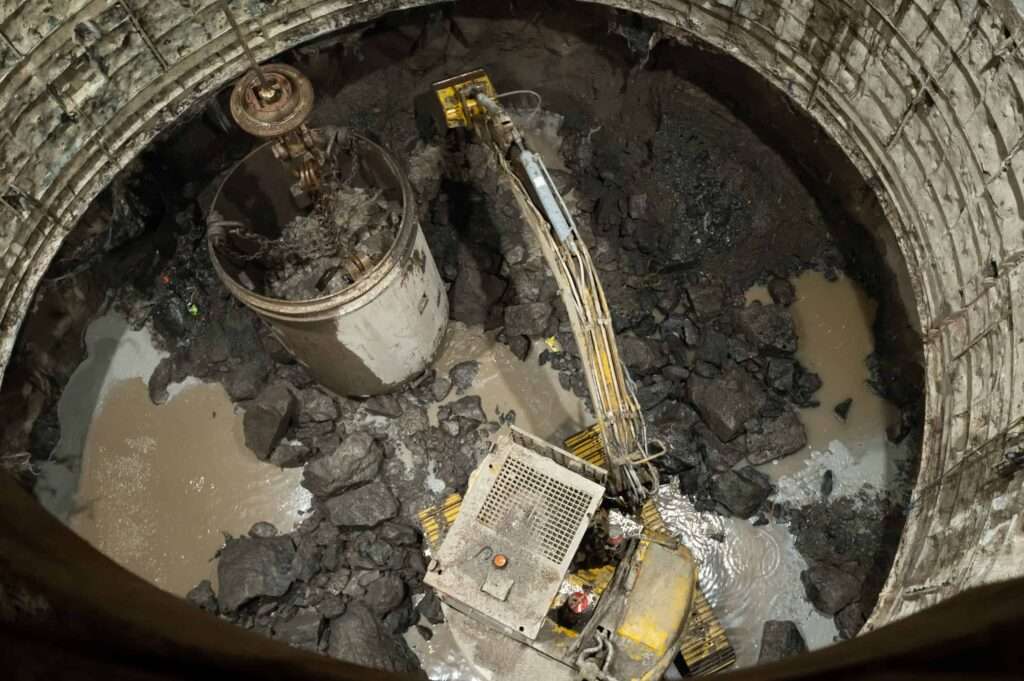 An excavator busy lashing at the shaft bottom with shaft lining being carried out on the face.